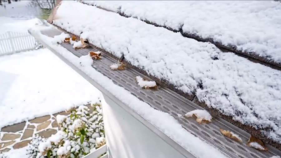 A gutter run photographed from the air in winter, snow along the roof edge and fallen leaves resting on the surface of the protection